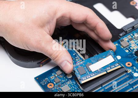 Computer technician installing laptop memory RAM in the slot of the motherboard. Stock Photo