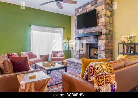 Vibrant, cozy, eclectic living room with stone fireplace, leather sofas, chairs, TV, and colorful decor Stock Photo