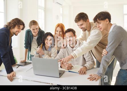 Cheerful young colleagues or students looking at laptop, discussing project and sharing ideas. Stock Photo