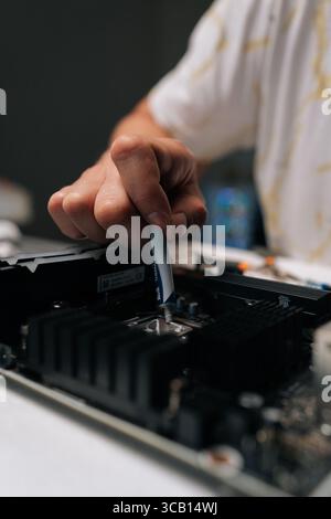 Vertical cropped shot technician applying thermal paste to CPU of computer motherboard, demonstrating process of computer maintenance and repair in Stock Photo