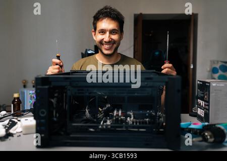 Friendly computer technician working with screwdrivers during desktop computer assembly, demonstrating technical expertise in workplace environment Stock Photo
