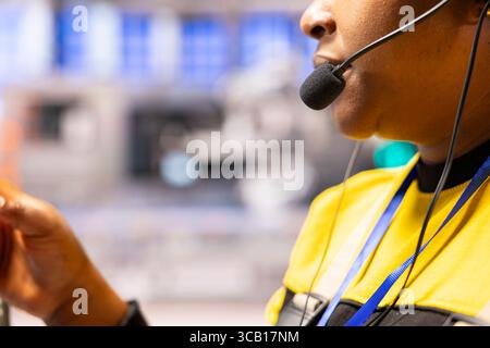 Closeup of engineer with headset monitoring automated factory conveyor belt and robotic arm operations, ensuring optimization and smooth functionality in smart manufacturing plant. Stock Photo
