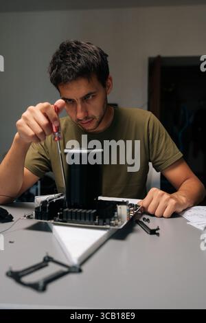 Vertical portrait of focused computer technician installing CPU cooler on motherboard with screwdriver, conducting maintenance and upgrades on desktop Stock Photo
