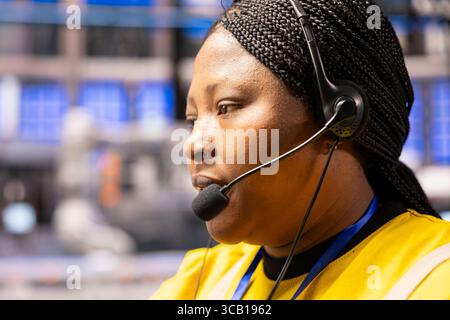 Black female engineer with headset communicates and monitors automation line in industry 4.0 facility, ensuring seamless operations in industrial plant. Technician oversees digital systems in factory. Stock Photo