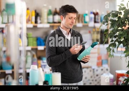 Middle-aged man scanning QR-code on cleaning spray at supermarket Stock Photo
