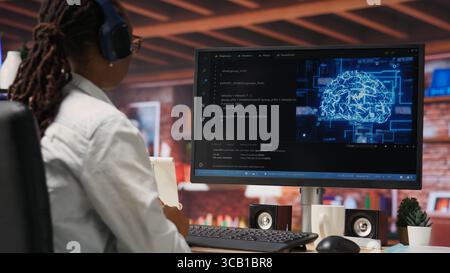 Admin doing maintenance on artificial intelligence neural networks computerized model, listening music. Tech support specialist wearing headphones doing checkup on AI systems, camera B Stock Photo