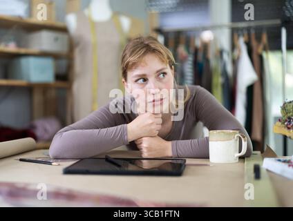 Thoughtful female fashion designer sitting at work table in studio Stock Photo