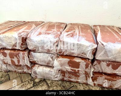 Stacks of packaged red clay blocks wrapped in plastic, ready for pottery or construction use. Stock Photo