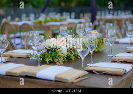 Wooden table decorated with crystal glasses and floral centerpiece, set outdoors for a wedding or elegant celebration. Stock Photo