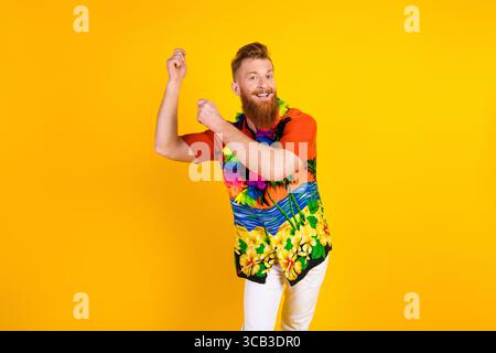 Cheerful bearded man in colorful tropical shirt dancing on a vibrant yellow background showcasing summer travel vibes Stock Photo