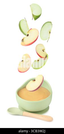 Baby food. Apple slices falling into bowl of puree on white background Stock Photo