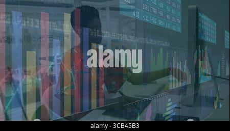 Analyst typing on keyboard using trackpad with laptop monitors and chart overlays at desk in office Stock Photo