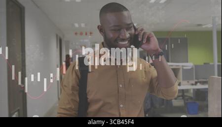 Walking man wearing mustard shirt and backpack through office hallway, speaking on smartphone Stock Photo