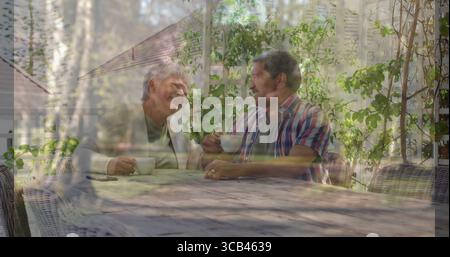 Sipping senior couple engaging in conversation at wooden table on garden patio, with ceramic cups Stock Photo