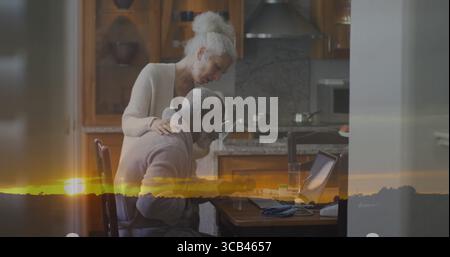 Collaborating couple working on laptop in kitchen area, with phone, papers, pen and glass of water Stock Photo