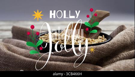 Showing black bowl of oats holding wooden scoop on cloth tabletop, with holly sprigs, text overlay Stock Photo