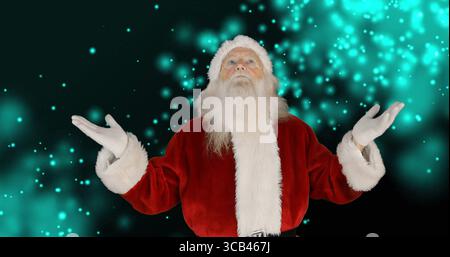 Standing Santa Claus figure raising arms against studio backdrop, with red coat and turquoise bokeh Stock Photo
