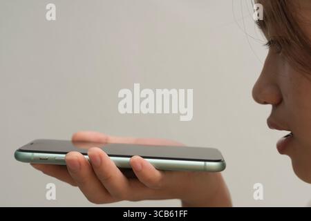 Close-up of young woman speaking into smartphone, using voice command or digital assistant. Concept of smart technology, AI interaction, hands-free co Stock Photo