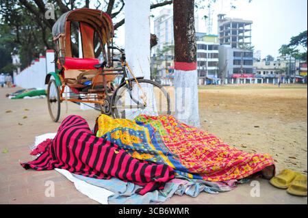 January 5, 2024: Sylhet-Bangladesh: Floating people sleep in the foggy winter  morning on the sidewalk next to the Sylhet Alia Madrasah grounds. Due to the increase in the prices of daily necessities, people are moving from poverty to more poverty, they are moving from villages to cities in search of work. The photo was taken early Friday morning. ....According to the population census in 2011 by the Bangladesh Bureau of Statistics (BBS), the Sylhet population was 479,837. The present population growth rate in Sylhet town is 2.5% per year. Considering 10% floating population comes to the city Stock Photo