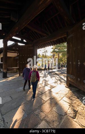 Two people walk through Nanzenji Sammon Gate, with warm afternoon sunlight casting long shadows on the stone pavement, Kyoto, Japan Stock Photo
