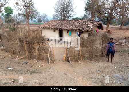 Local man standing in front of his traditional handmade house made from mud, fence made from branches in Chhattisgarh in india Stock Photo