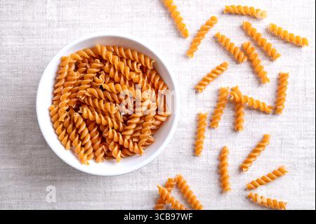 Chickpea spiral pasta, gluten free noodles in a white bowl on linen fabric. Small fusilli, a pasta variety, with helical or corkscrew shape. Stock Photo