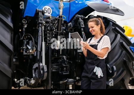 Female agricultural mechanic using digital tablet near farm tractor Stock Photo