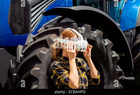 Modern female farmer exploring virtual reality farming solutions near tractor outdoors in country. Stock Photo