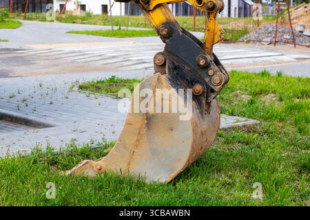 A vibrant yellow excavator bucket is currently positioned on the grassy area, showcasing its robust construction and machinery features Stock Photo