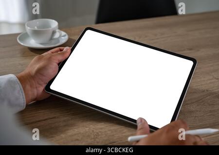 Blank screen concept represented by a person holding a digital tablet with a white display and stylus in a modern workspace, ready for content creatio Stock Photo