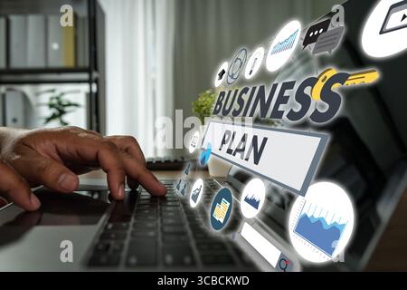 Business plan concept represented through digital icons and charts as a person types on a laptop in a workspace, developing strategy and analyzing dat Stock Photo