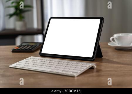 Digital workspace mockup concept featuring a blank tablet screen with wireless keyboard, calculator, and coffee cup as a person prepares to work or de Stock Photo