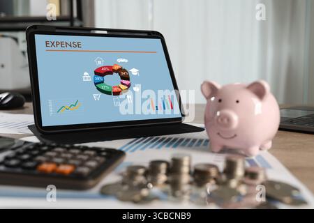 Expense analysis concept shown through colorful financial charts on a tablet screen as a person manages personal budgeting with coins, piggy bank, and Stock Photo