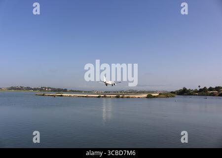 Low-flying airplane approaching Corfu for landing over the sea, seen during final descent near the coastline Stock Photo