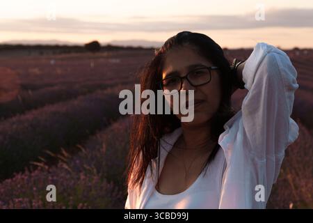 A woman wearing glasses and a white shirt stands in a field of lavender. She is looking at the camera Stock Photo