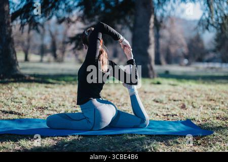 Woman practicing advanced yoga poses on a mat in a peaceful park Stock Photo