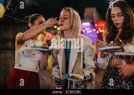 Young women sharing cake during a lively backyard birthday celebration at night Stock Photo