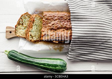 Zucchini and cheese bread recipe, a loaf of bread on a wooden cutting board, covered with a kitchen towel, with a whole zucchini vegetable next to it. Stock Photo
