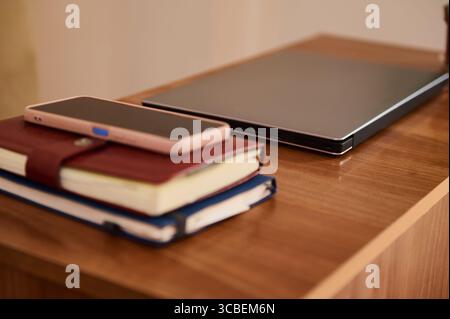 Organized workspace featuring closed laptop, smartphone, and two notebooks on a wooden table. Evoking professionalism and preparation, this setting is Stock Photo