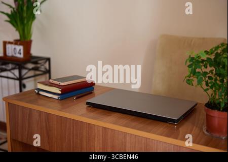 A cozy workspace featuring a wooden desk with a sleek laptop, books, and a smartphone, surrounded by potted plants and natural decor. Perfect for a pr Stock Photo