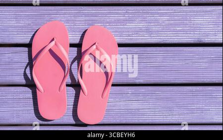 Pink flip flops are placed on a sunlit purple wooden deck, suggesting a relaxed summer atmosphere. The vibrant colors create a cheerful and inviting s Stock Photo
