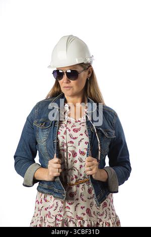 Forty something woman, wearing casual clothes, hard hat and sunglasses, holding her demin jacket Stock Photo