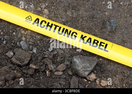 Gelbes Flatterband mit schwarzer Aufschrift ACHTUNG KABEL liegt in einem aufgebaggertem Loch in der Gosenbacher Str. Derzeit wird in Siegen-Oberschelden Glasfaserkabel verlegt. Glasfaserkabel am 08.08.2025 in Siegen/Deutschland. *** Yellow flutter tape with black lettering ATTENTION CABLE is lying in an excavated hole in Gosenbacher Str Fiber optic cable is currently being laid in Siegen Oberschelden Fiber optic cable on 08 08 2025 in Siegen Germany Stock Photo