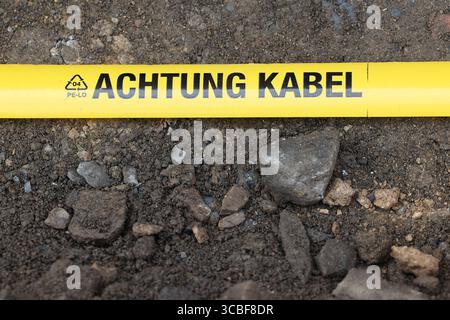 Gelbes Flatterband mit schwarzer Aufschrift ACHTUNG KABEL liegt in einem aufgebaggertem Loch in der Gosenbacher Str. Derzeit wird in Siegen-Oberschelden Glasfaserkabel verlegt. Glasfaserkabel am 08.08.2025 in Siegen/Deutschland. *** Yellow flutter tape with black lettering ATTENTION CABLE is lying in an excavated hole in Gosenbacher Str Fiber optic cable is currently being laid in Siegen Oberschelden Fiber optic cable on 08 08 2025 in Siegen Germany Stock Photo