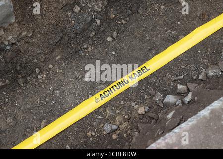 Gelbes Flatterband mit schwarzer Aufschrift ACHTUNG KABEL liegt in einem aufgebaggertem Loch in der Gosenbacher Str. Derzeit wird in Siegen-Oberschelden Glasfaserkabel verlegt. Glasfaserkabel am 08.08.2025 in Siegen/Deutschland. *** Yellow flutter tape with black lettering ATTENTION CABLE is lying in an excavated hole in Gosenbacher Str Fiber optic cable is currently being laid in Siegen Oberschelden Fiber optic cable on 08 08 2025 in Siegen Germany Stock Photo