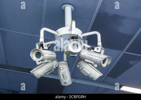 Cluster of multiple security cameras mounted on a ceiling for surveillance in a modern building environment singapore MRT metro  CBD Stock Photo