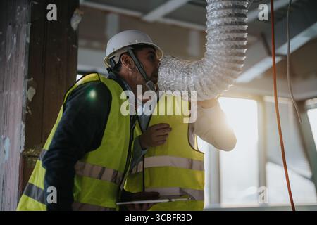 Construction workers inspecting air duct installation at building site Stock Photo