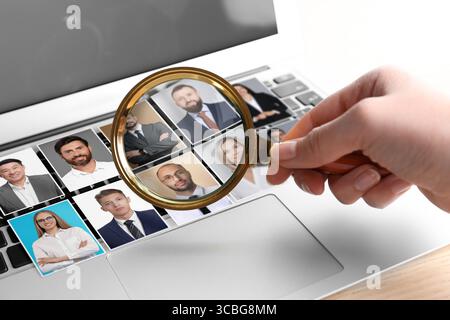 Recruiter looking at candidates' photos through magnifying glass on laptop, closeup. Human resources management Stock Photo