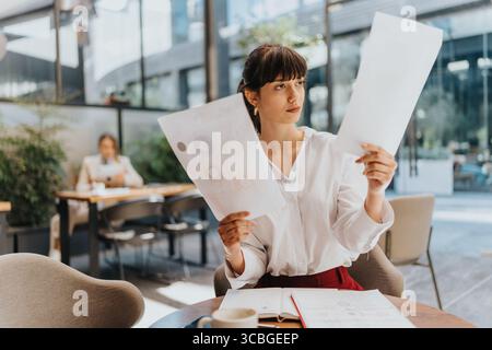 Focused young businesswoman analyzing documents in a modern cafe setting Stock Photo