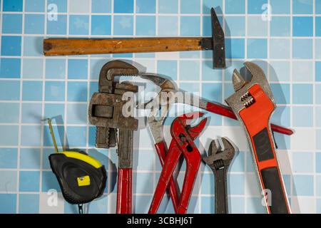 Different plumbing tools are lying on blue bathroom tiles, ready for a plumber to use them Stock Photo